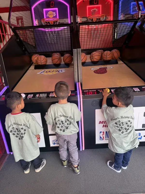 Three boys in Hogar's Helping Hands shirts at the arcade