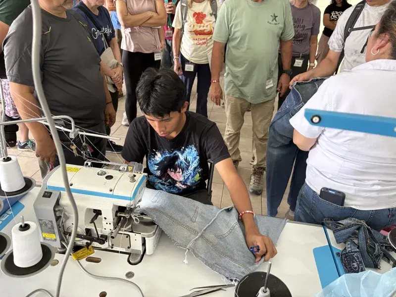 A student at the sewing machine while visitors look on