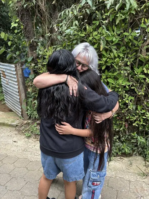 A volunteer embracing two girls at the end of the week